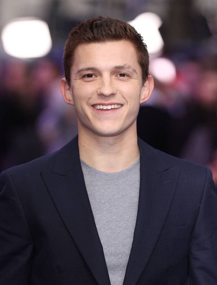 Tom Holland smiles for the camera while wearing a suit and shirt