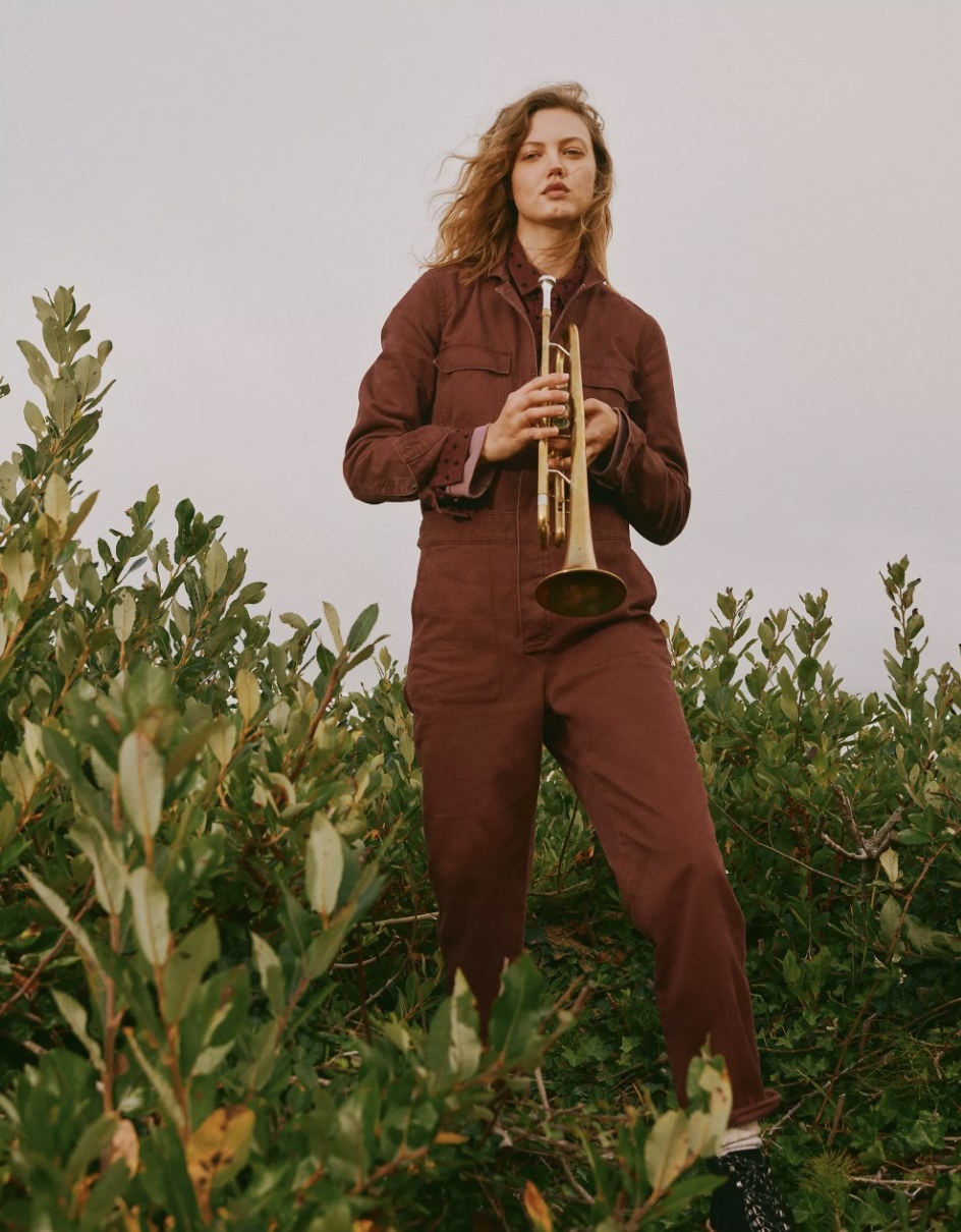 Model wearing the coveralls in a field while posing with her trumpet