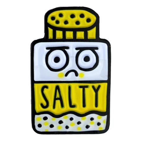 an enamel pin of a salt shaker with a sad face that reads salty