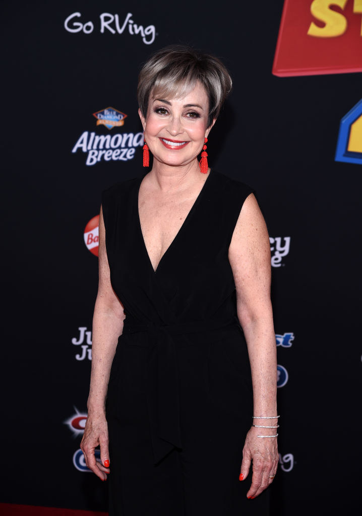 Woman wearing black dress, with short blonde hair and dangly orange earrings.