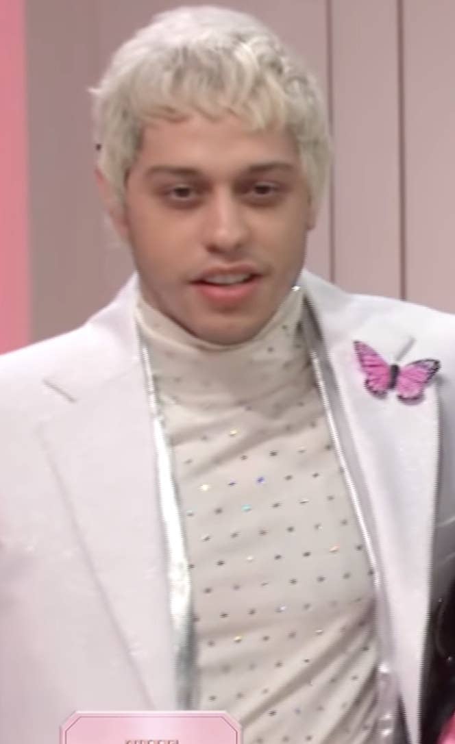 Davidson with bleached hair while wearing a light colored suit with a butterfly attached