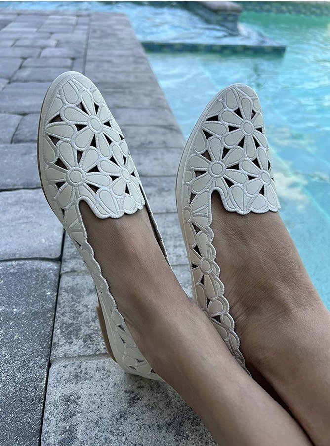 A reviewer wearing white floral flats near a pool