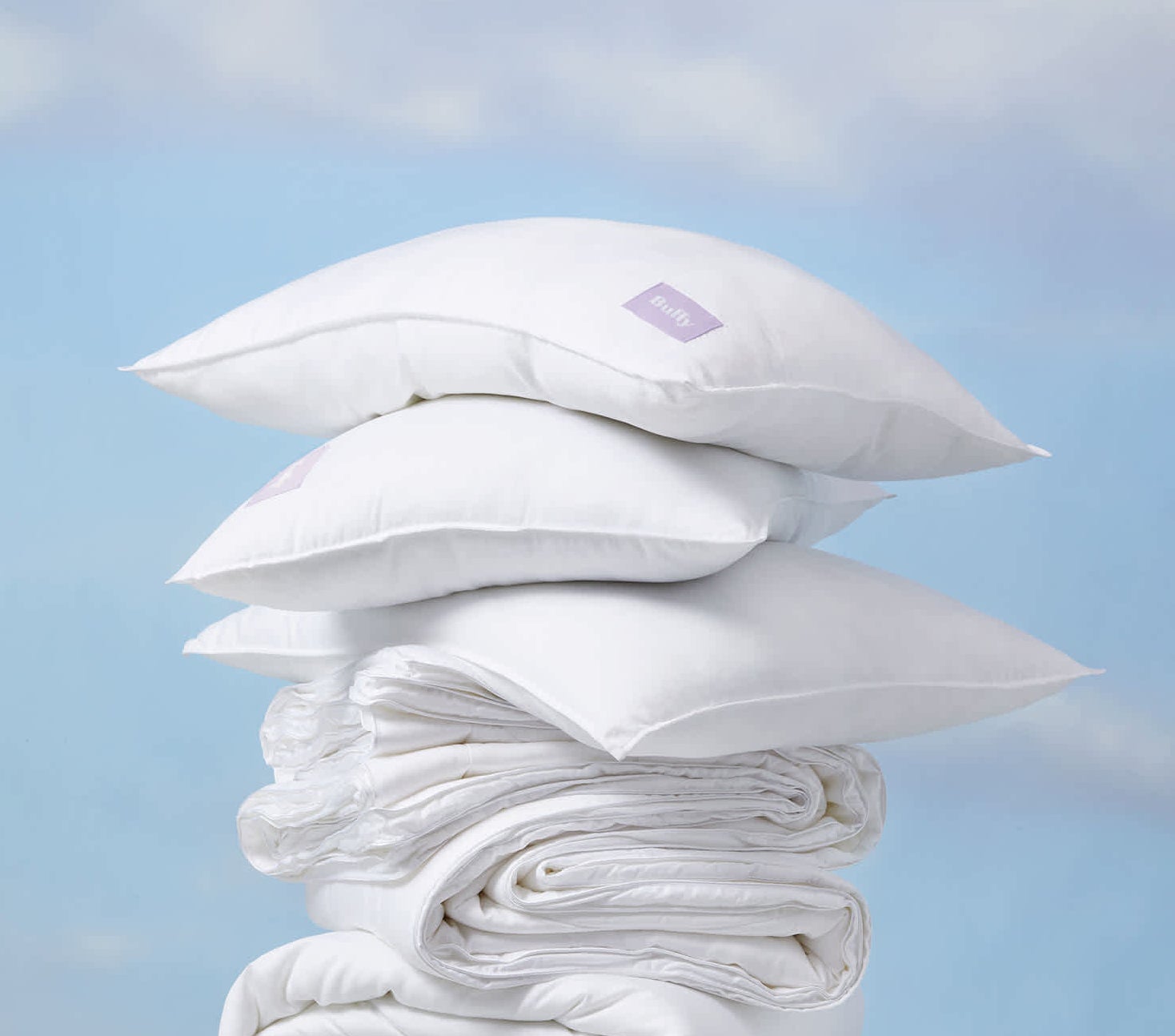 a stack of pillows on top of a stack of comforters