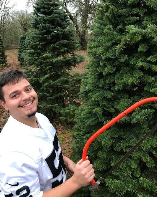 Commenter&#x27;s husband posing with saw next to Christmas trees