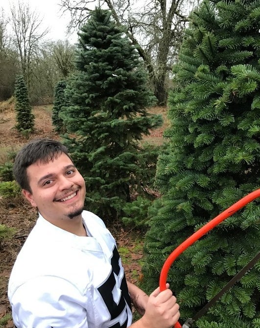 Commenter&#x27;s husband posing with saw next to Christmas trees