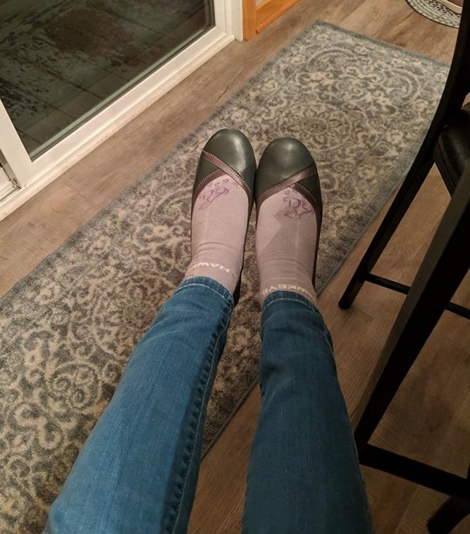 A reviewer wearing green and brown flats with pink socks and medium wash denim