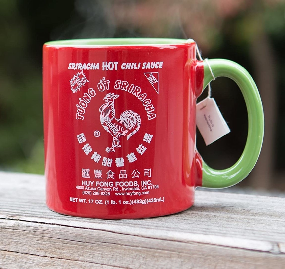 The red and green Sriracha mug holding a tea bag outdoors