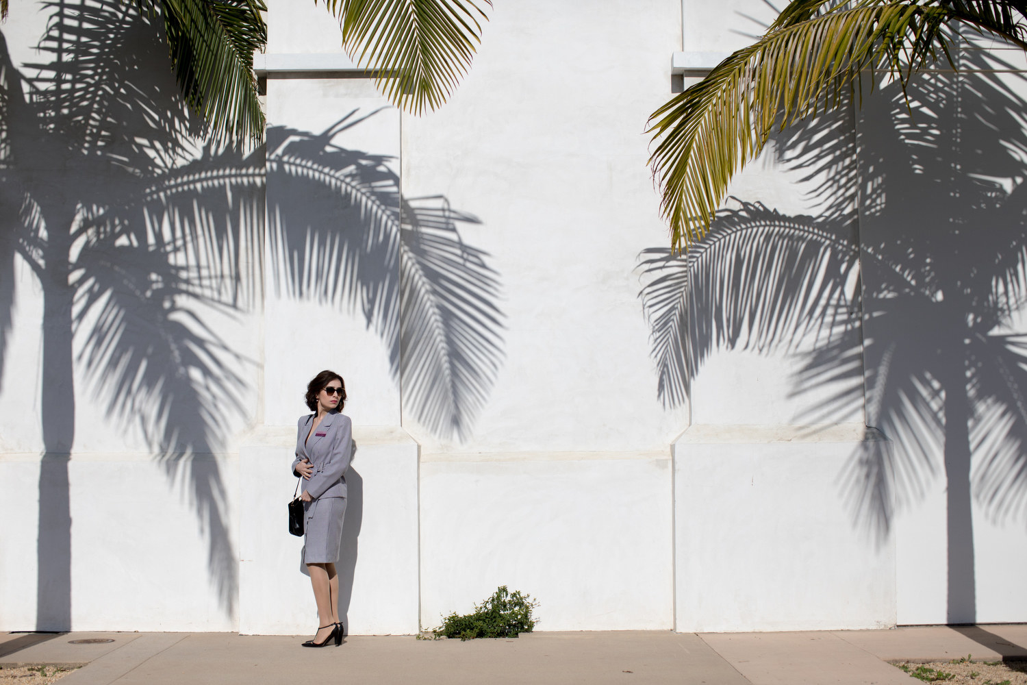 A woman in a skirt and blazer outside under palm trees