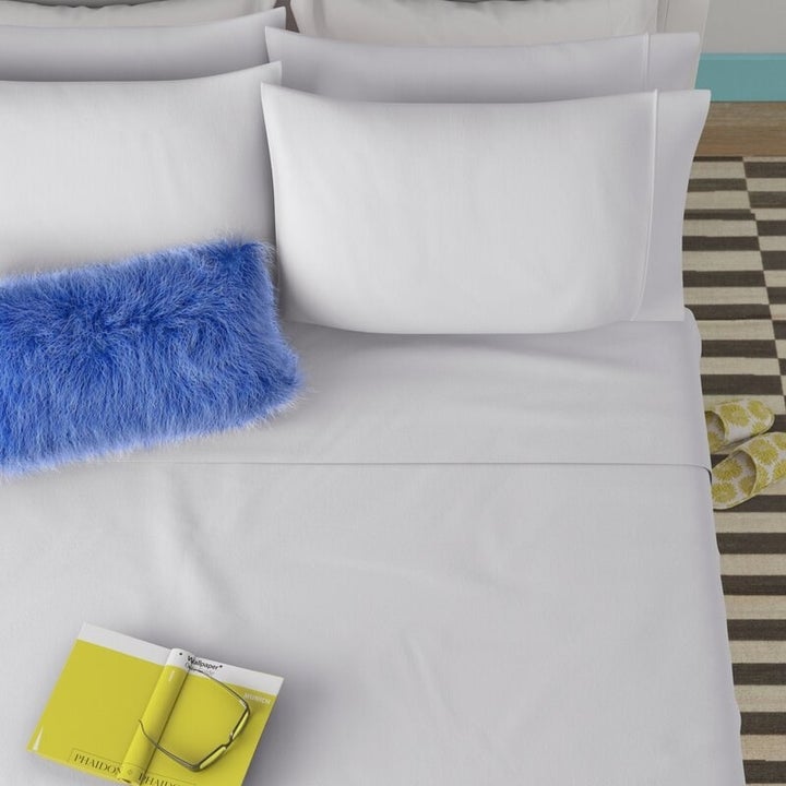 White sheets on a bed with blue pillow and green book