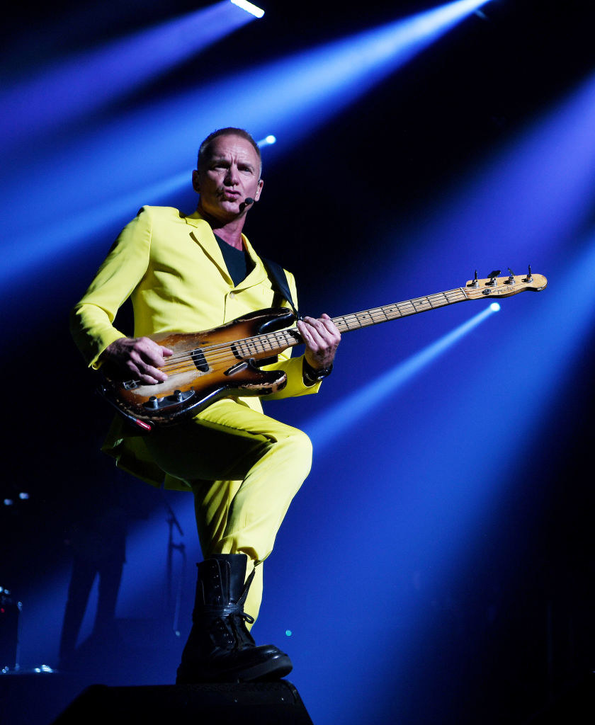 The musician playing bass onstage in a light yellow suit and a black stop