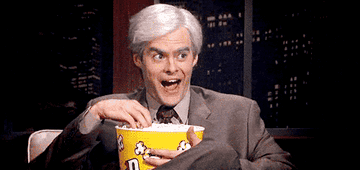 Man looks excited while eating out of a tub of popcorn