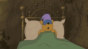gif if winnie the pooh in a sleep mask and cap snuggling with his pillow