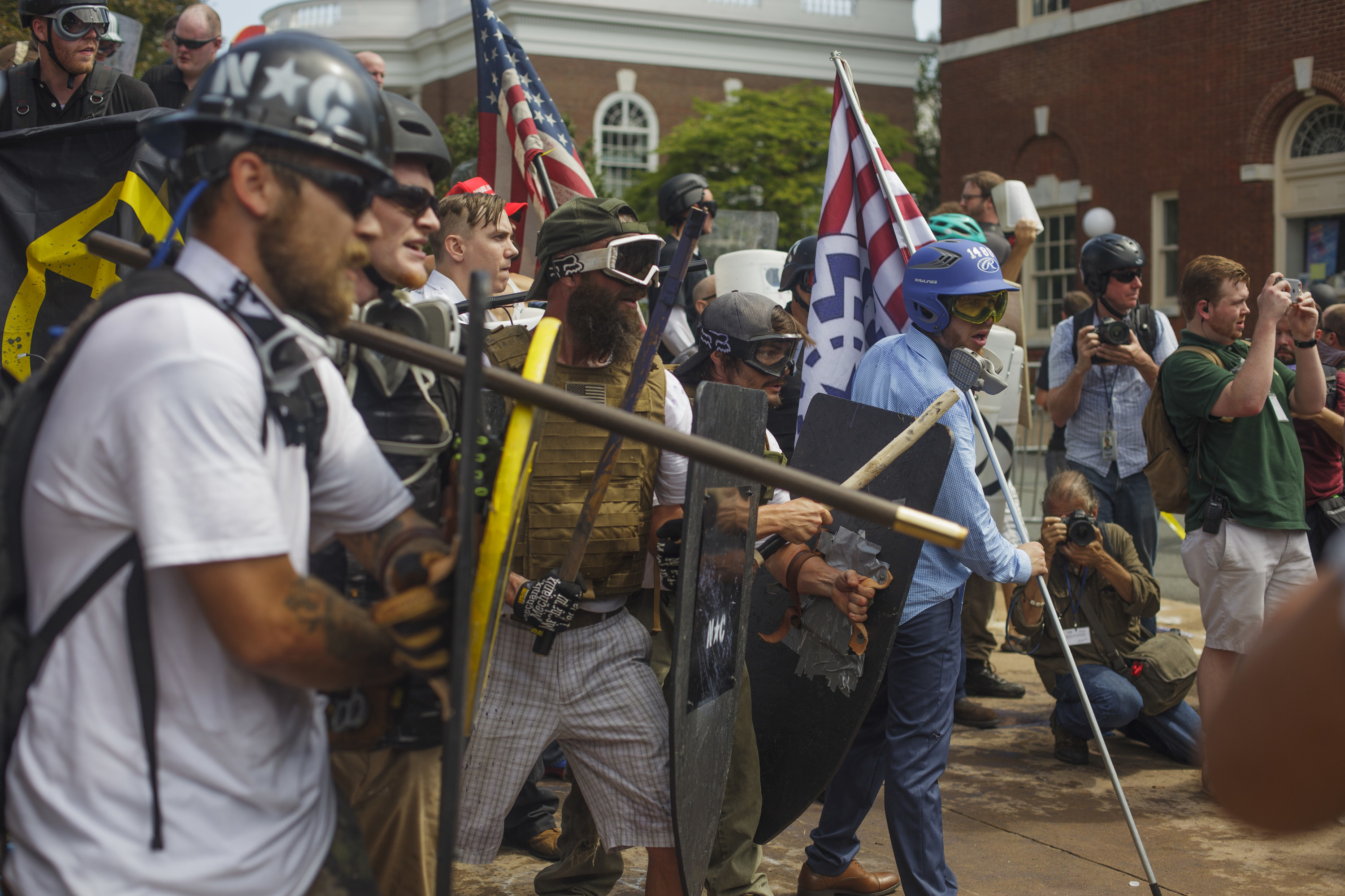 People wear riot gear and hold up shields and bats outside