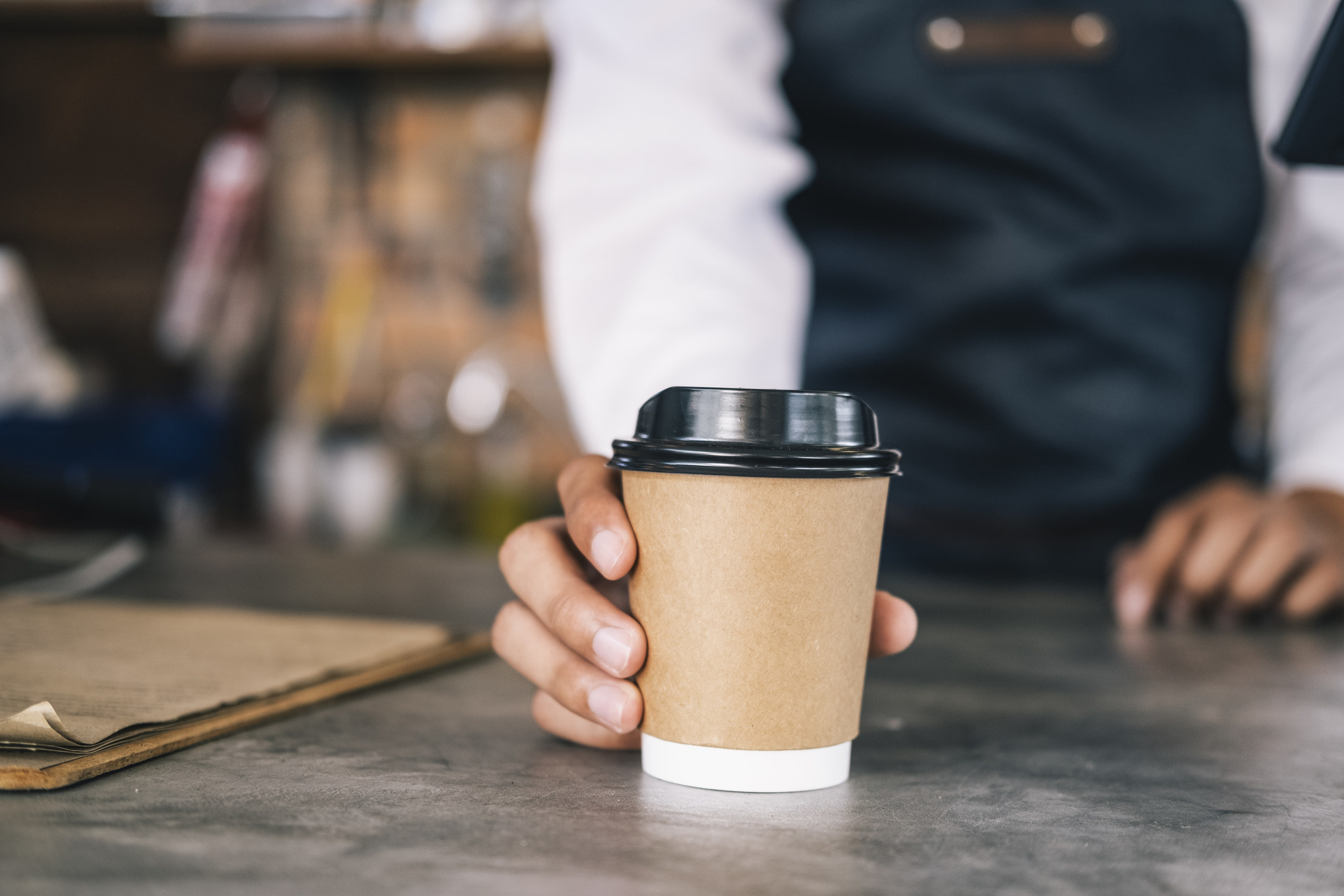 A person holding a covered cup of coffee to go