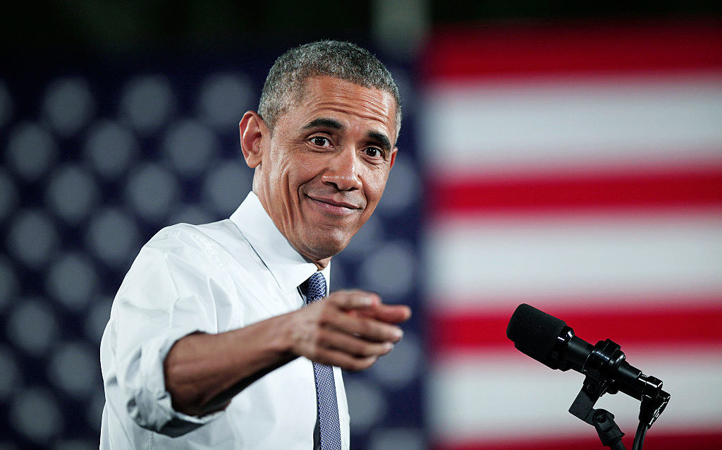 Barack with rolled-up sleeves and wearing a tie at a microphone