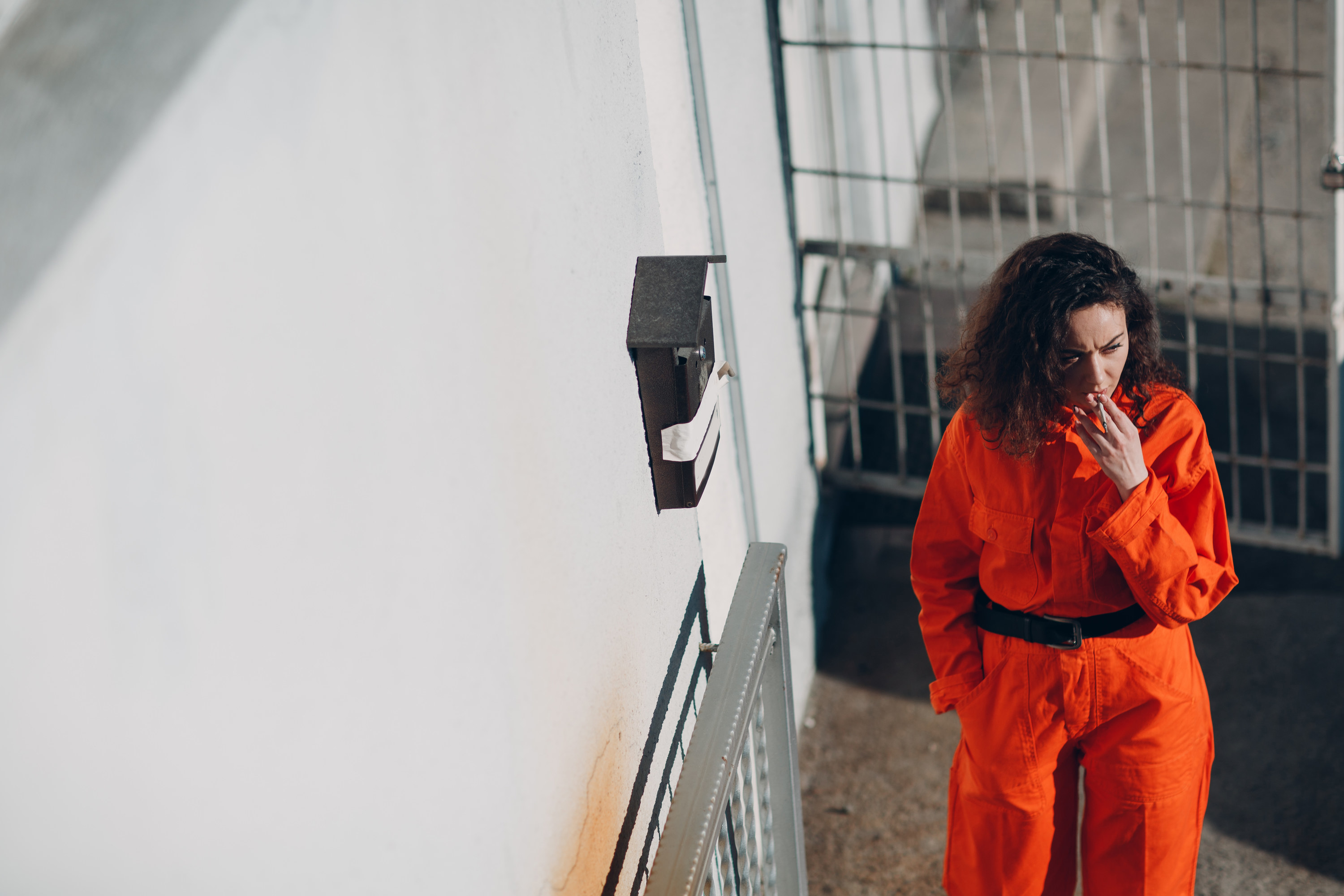 Woman wearing an orange prison jumpsuit stands by a phone