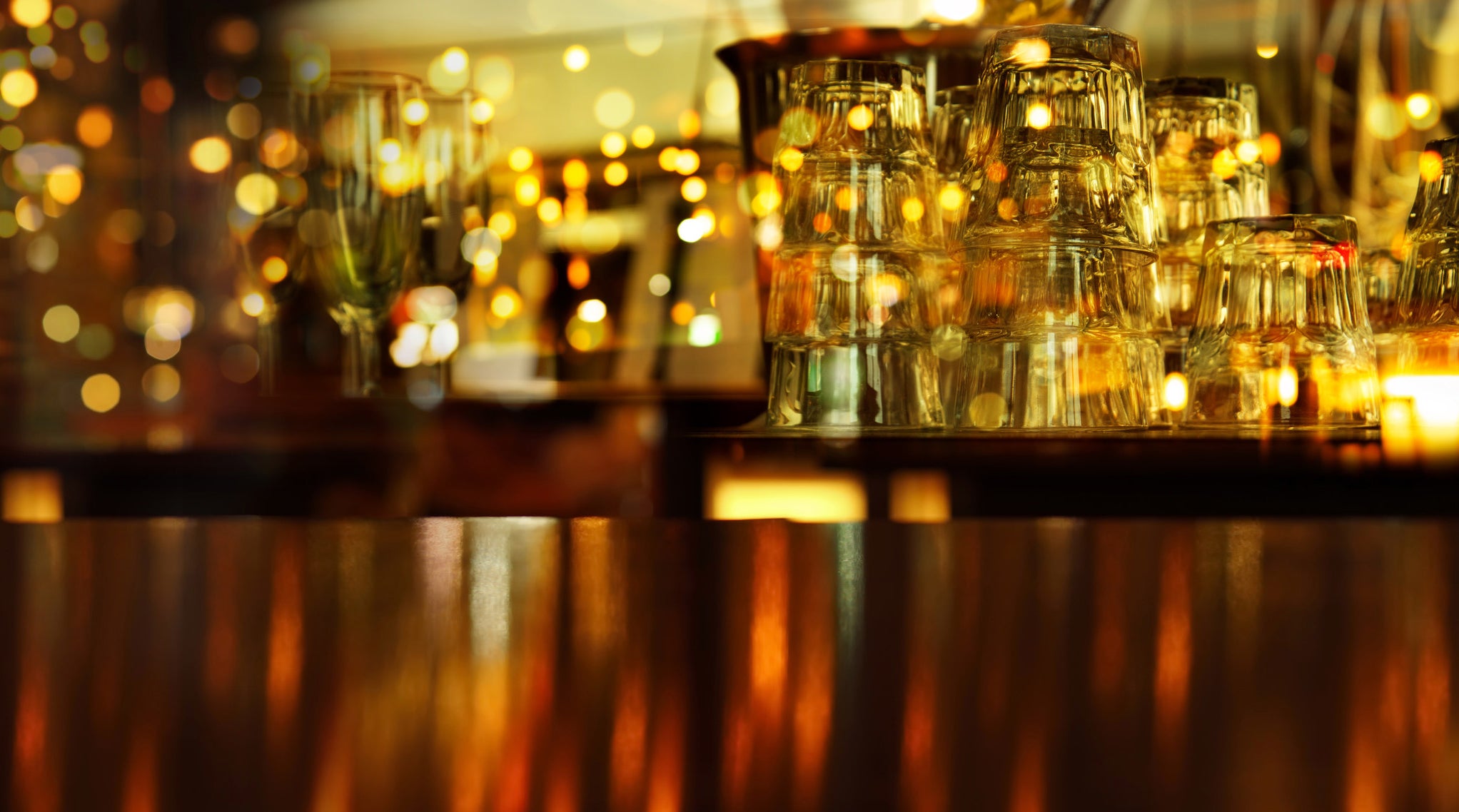 glasses sitting on a shelf in a bar with holiday lights reflecting off of them