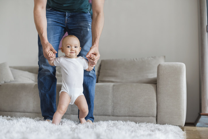 Someone holding a baby up while they try to walk