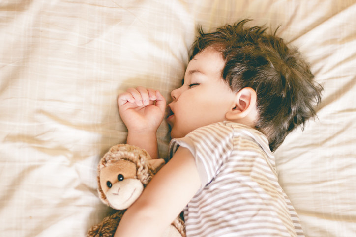 Boy sleeping on bed holding a soft toy by his side