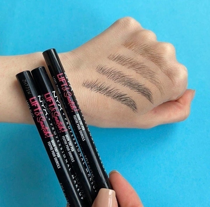 a person holding up three brow pens with tiny hair strokes drawn on their hand