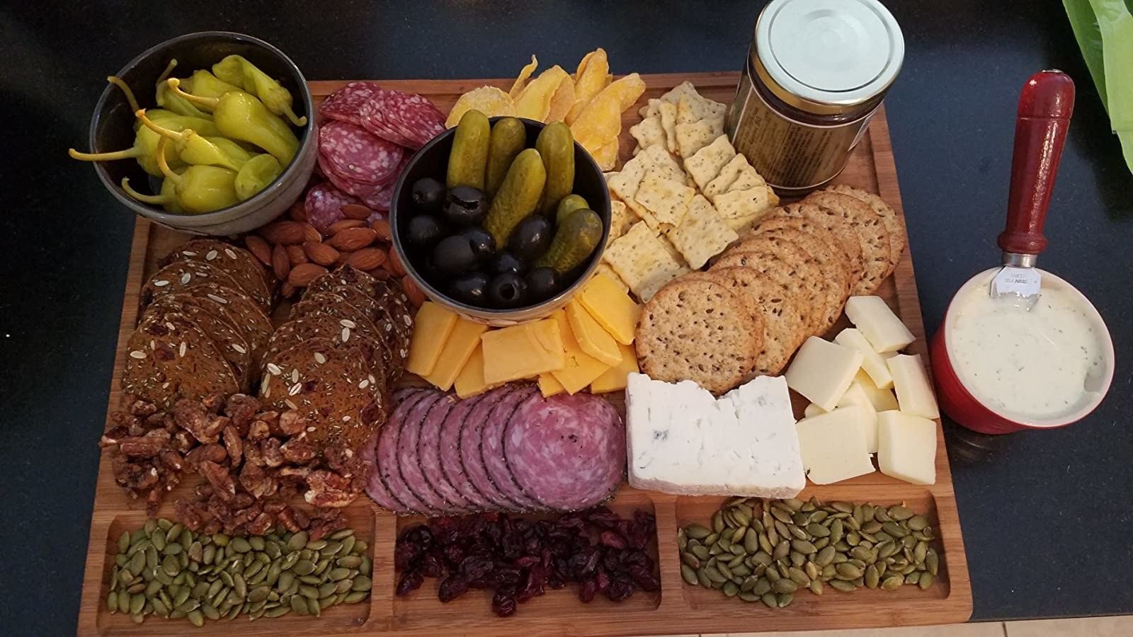A reviewer&#x27;s board with nuts in the grooves, and many cheese, crackers, and snacks