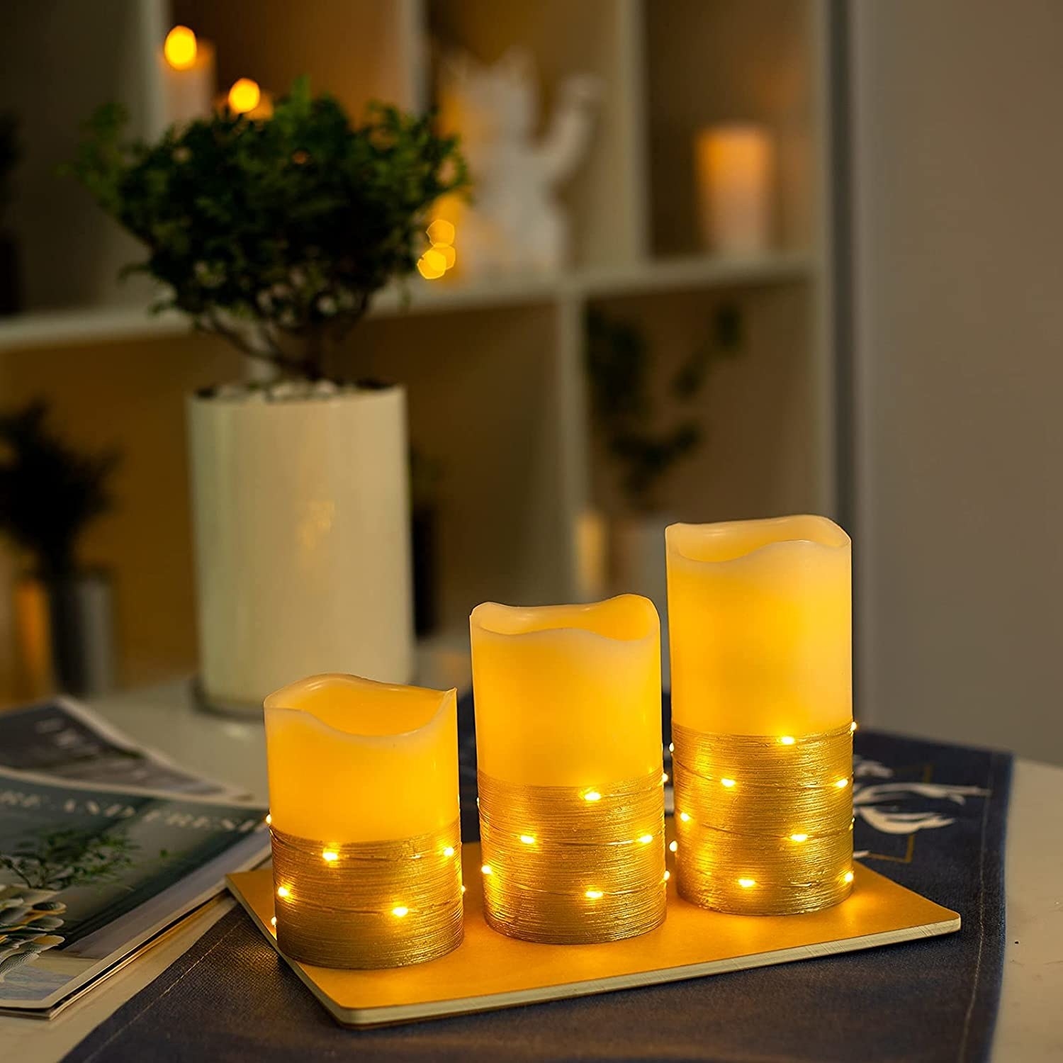 The three candles in different heights on a tray with gold bottoms and string lights