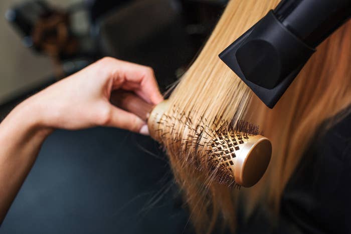 Close-up of a hairdresser&#x27;s hand drying blonde hair with a hair dryer and round brush
