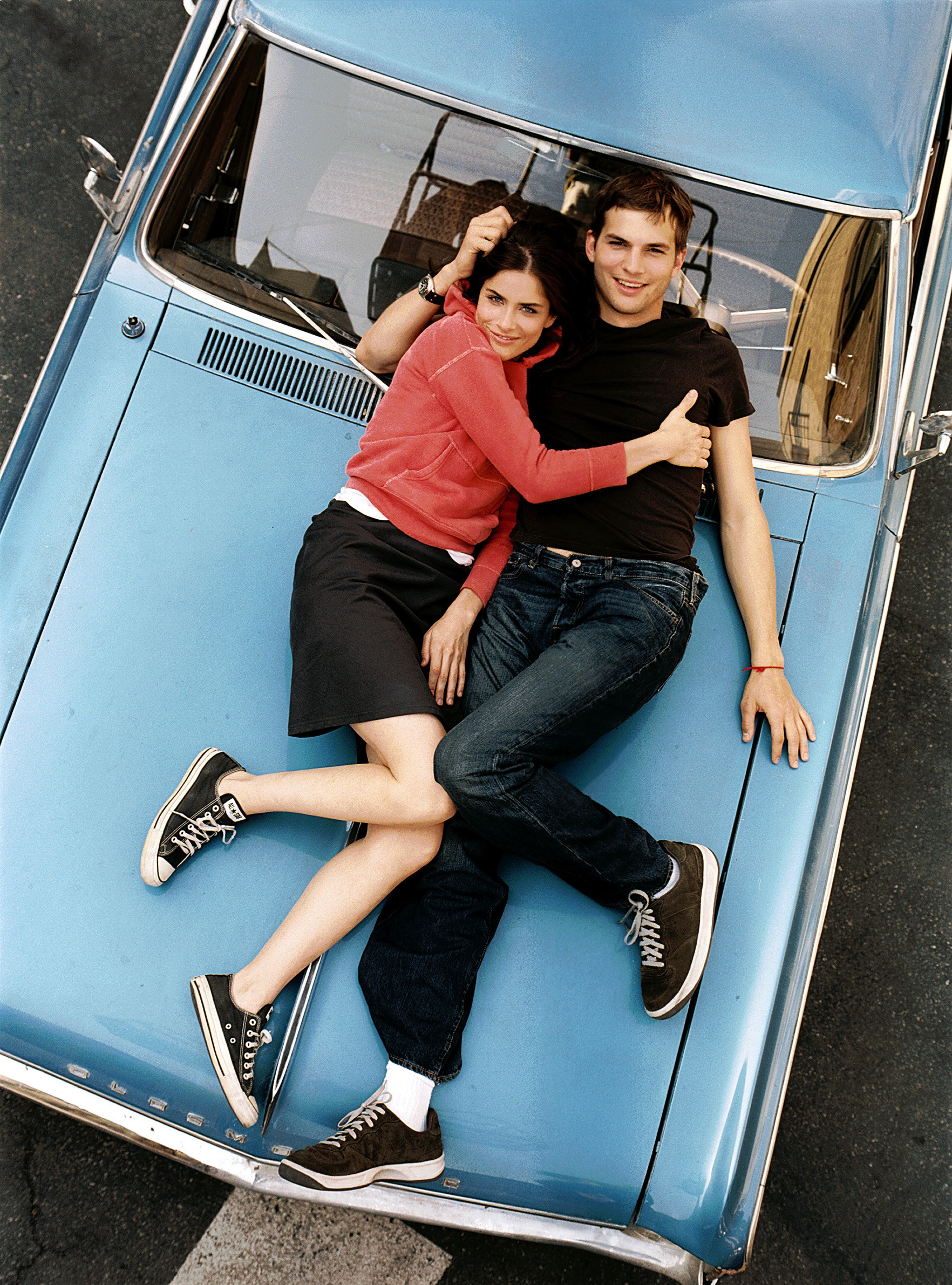 Amanda Peet and Ashton Kutcher look up while lying on the bonnet of a car.
