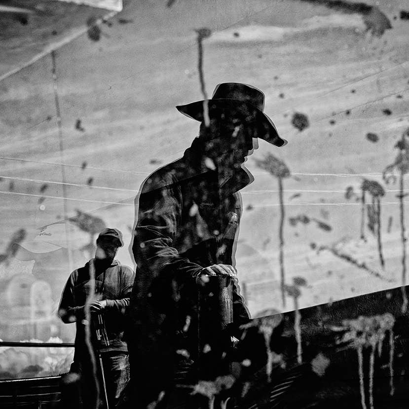 An image of a man wearing a cowboy hat is blurry and reflected in a window