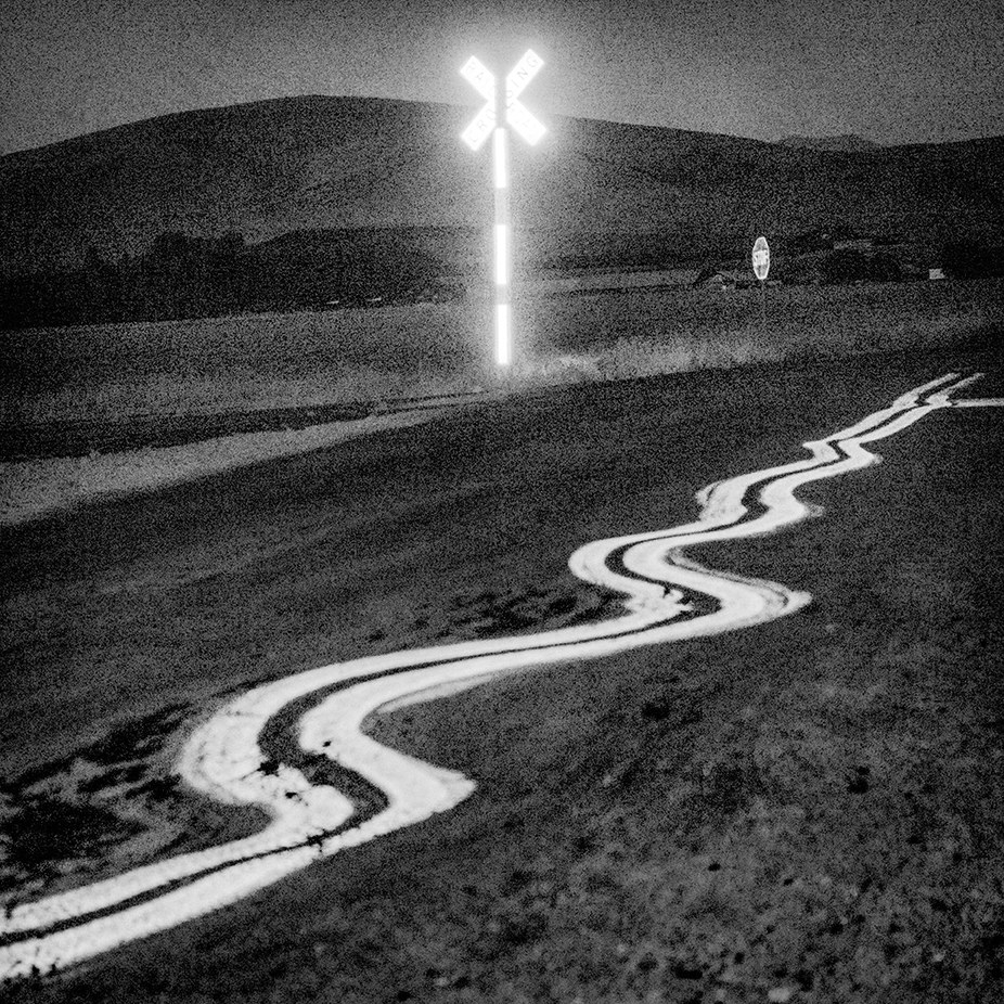 A road zig-zags from the foreground into the distance near a glowing reflective railroad crossing sign