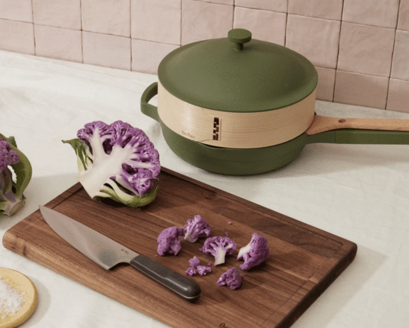 The cutting board with cauliflower on it in front of an Always Pan