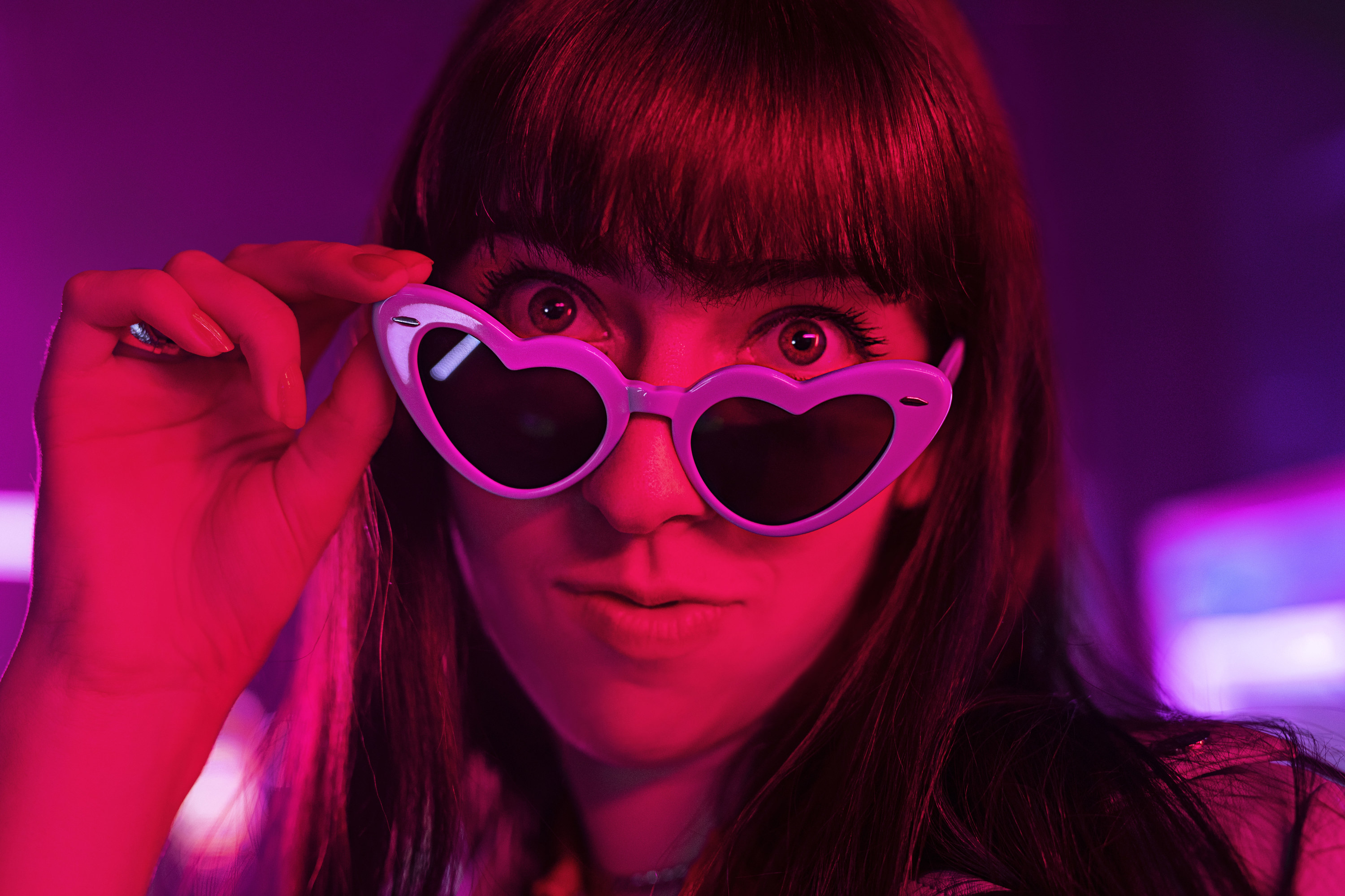 A woman peers over heart-shaped sunglasses.