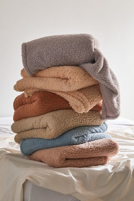 stack of different colored fleece blankets on a bed