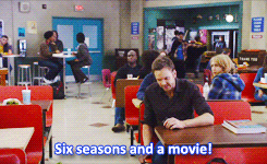 Jeff sitting in the cafeteria while Abed plays with a cape in the background in &quot;Community&quot;
