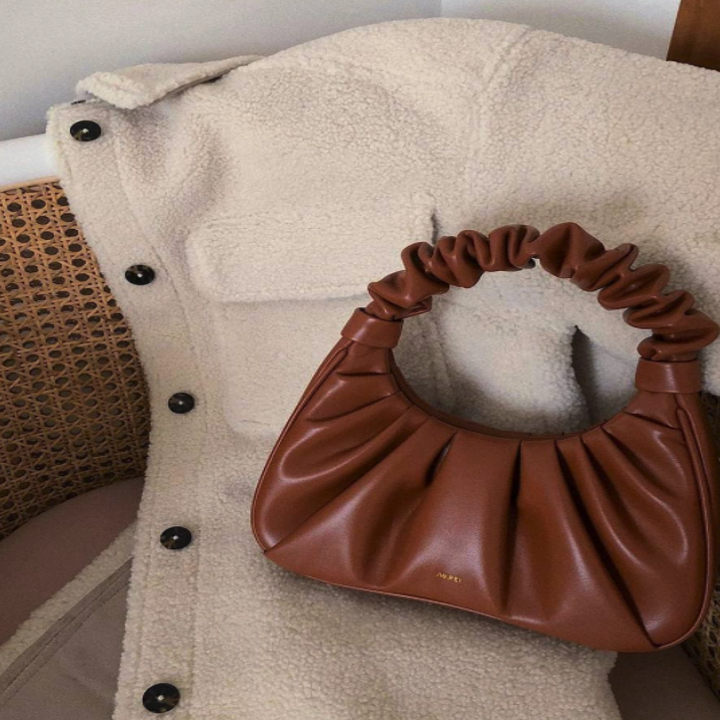 the bag in brown laying flat against a jacket, showing the JW Pei logo in front