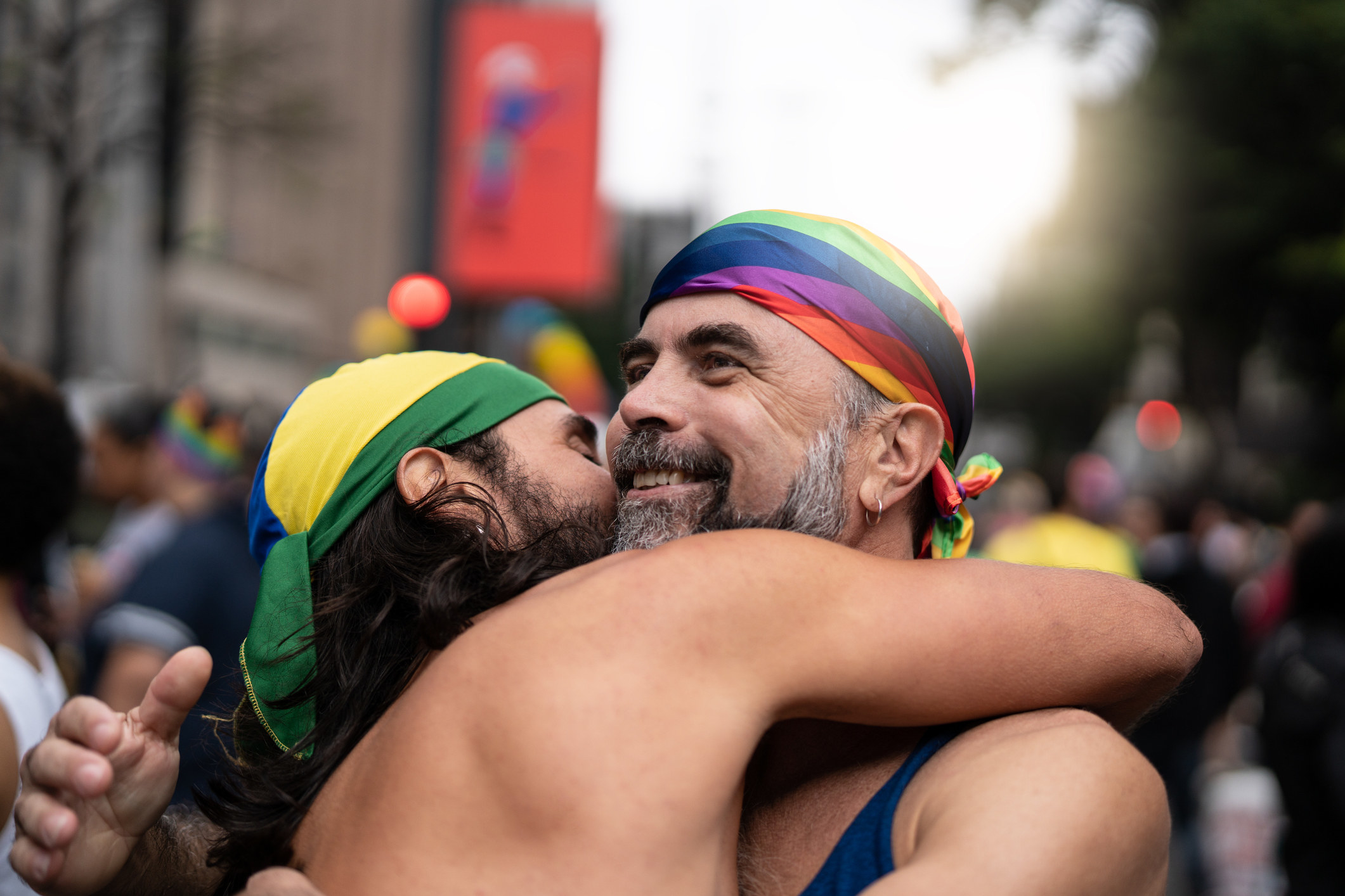 Gay man with gray beard is embraced by a younger gay during a Pride event