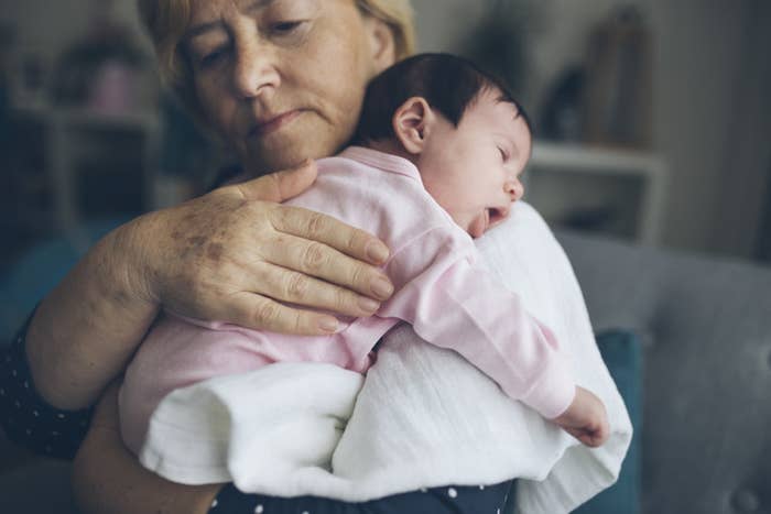 An older woman holding a sleeping baby on her shoulder