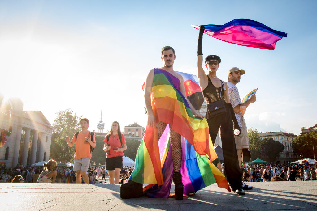 A pair of queer people flaunt the rainbow and bisexual flag at Milan Gay Pride held at the Arco della Pace