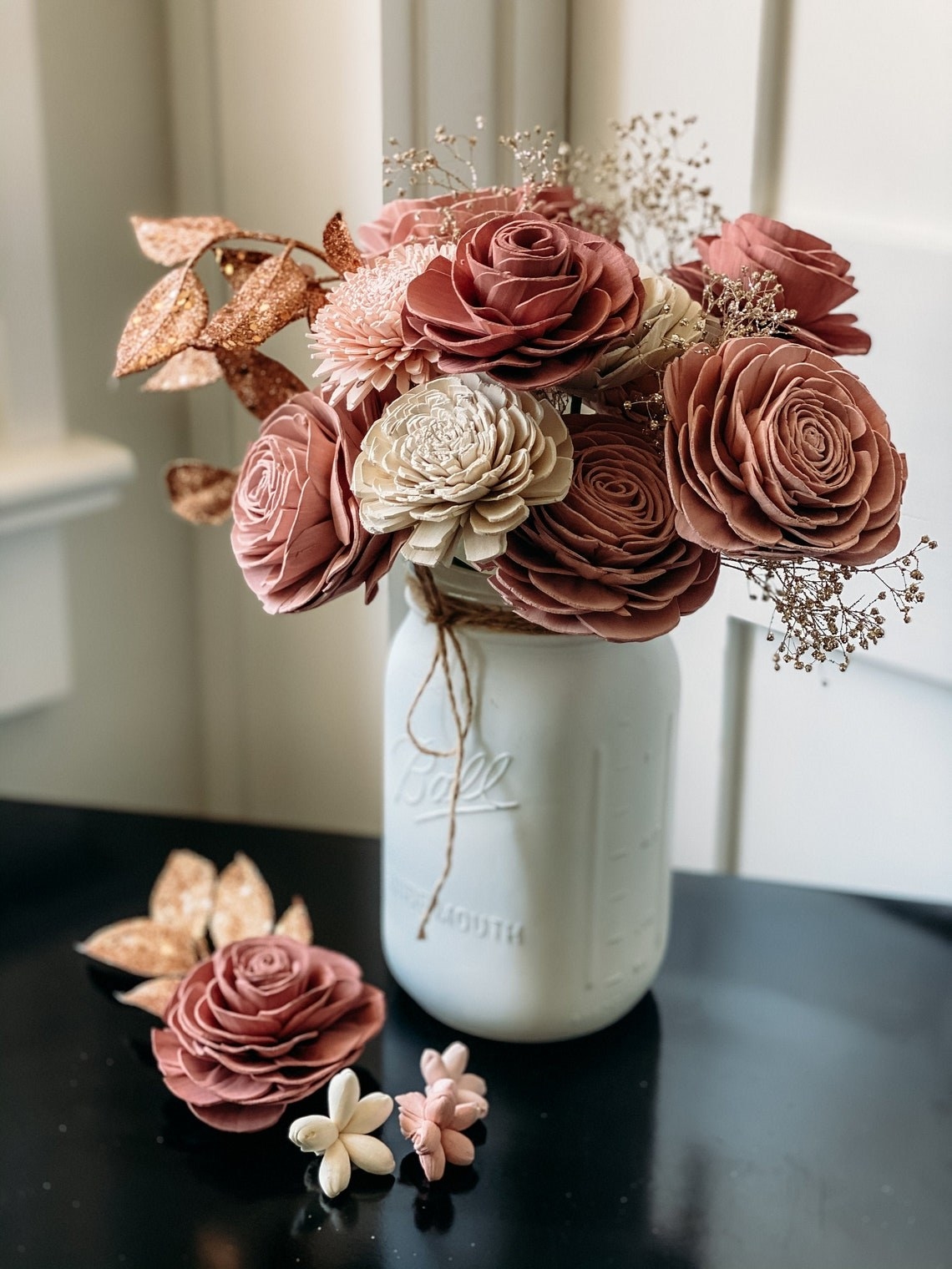 A bouquet of ivory, pink, and rose gold wooden flowers in a white Mason jar