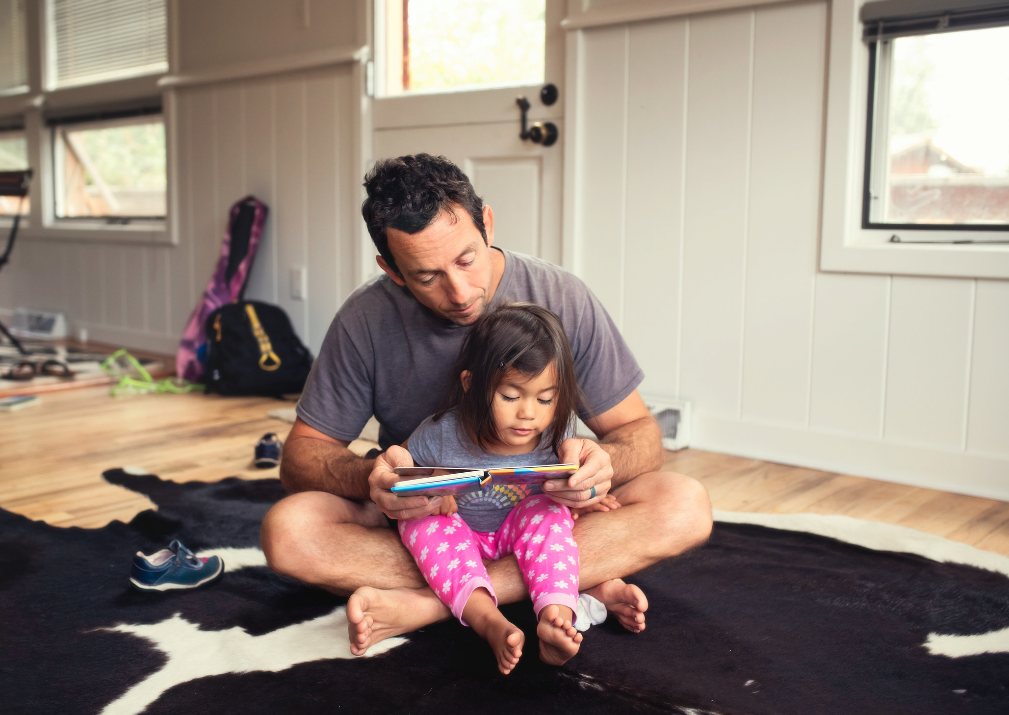 A middle age father sits with his young daughter on the floor, teaching her to read