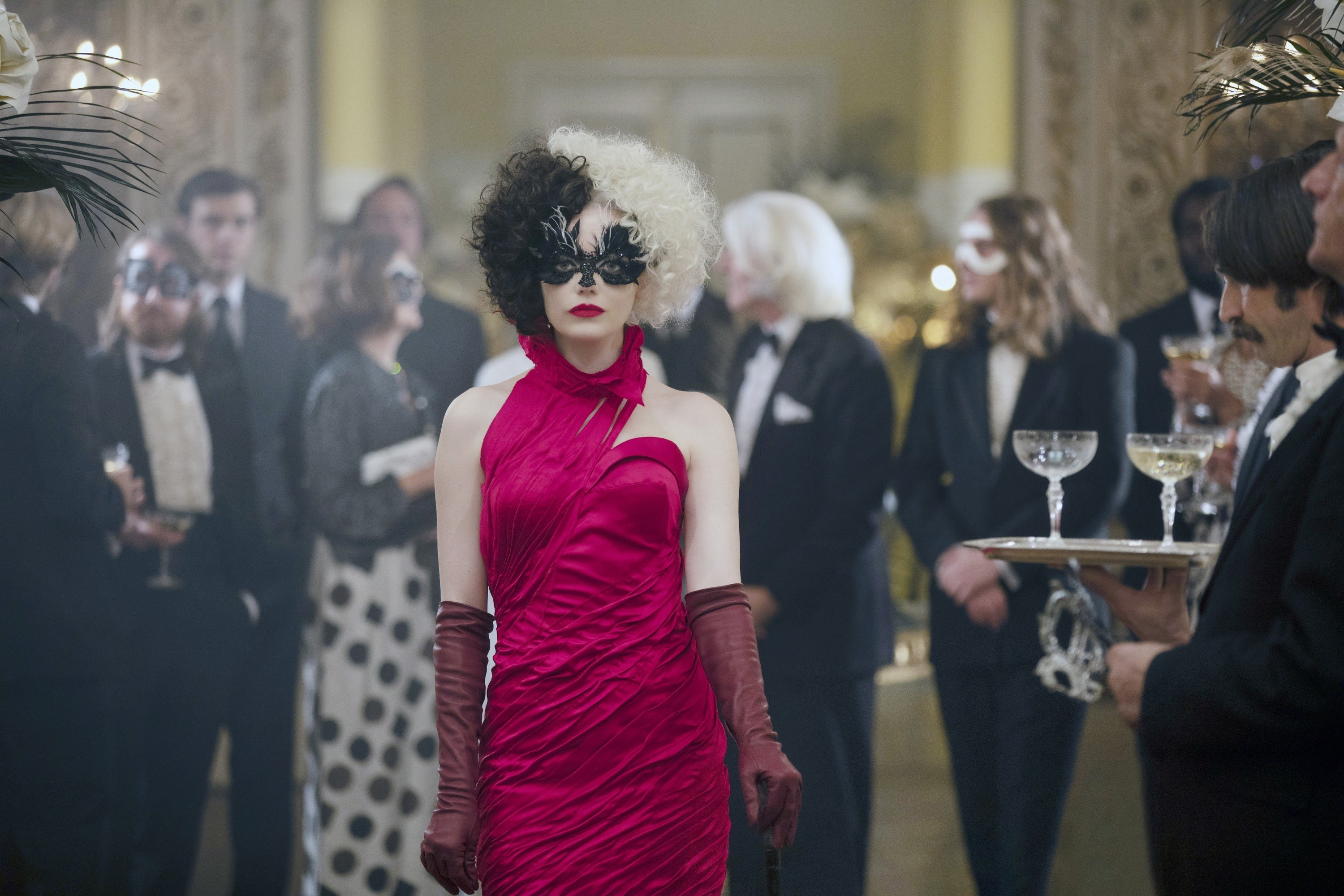 Cruella wearing a gown and long gloves and standing in a crowd