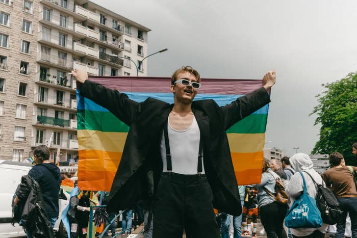 A person in a blazer and suspenders holds up a Pride flag during the 2021 Paris Pride Parade