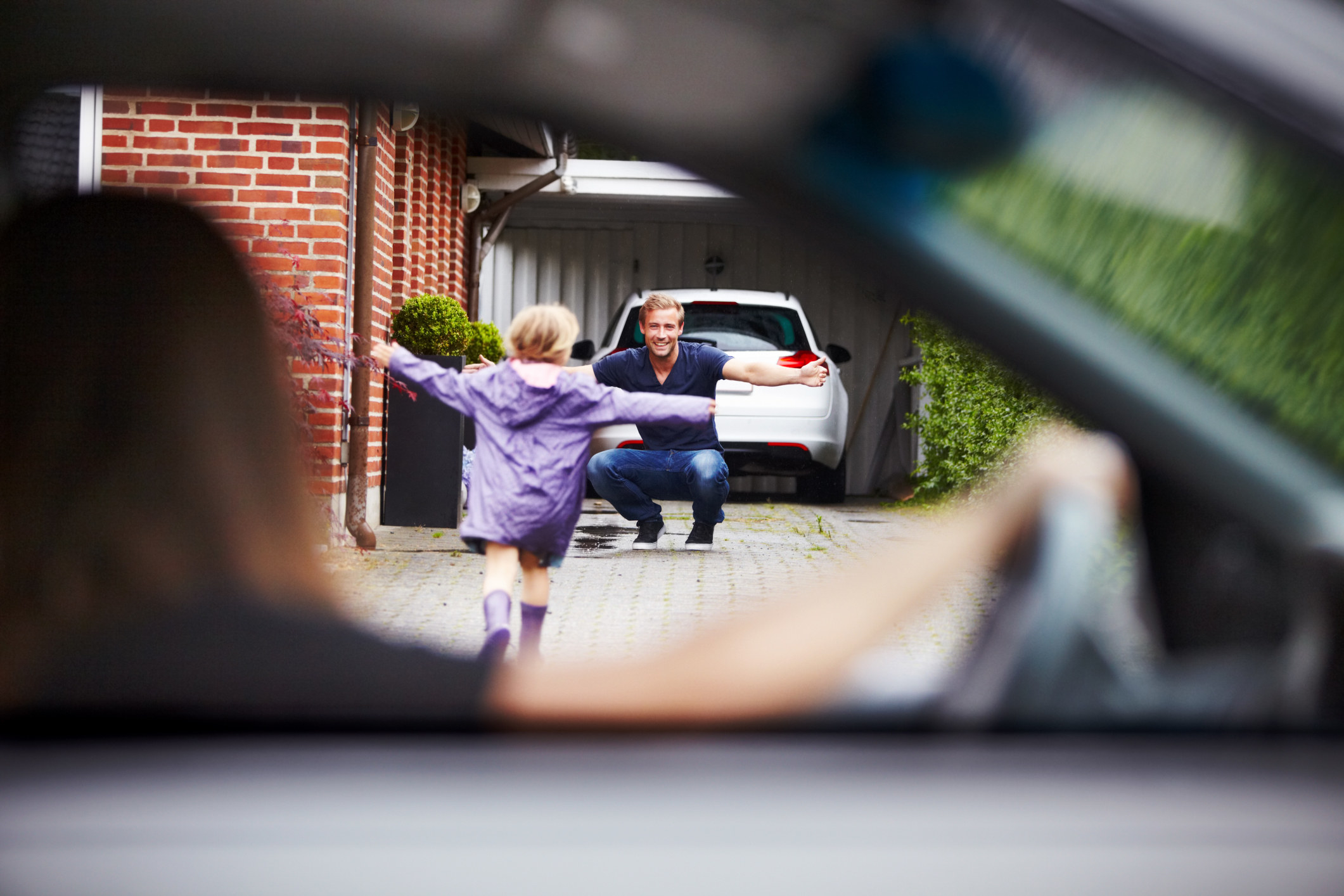 Mother watches from the car as her daughter runs towards her father with open arms