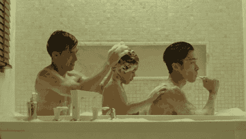 A father shampoos his son&#x27;s hair while his son washes his other father&#x27;s back in a bathtub