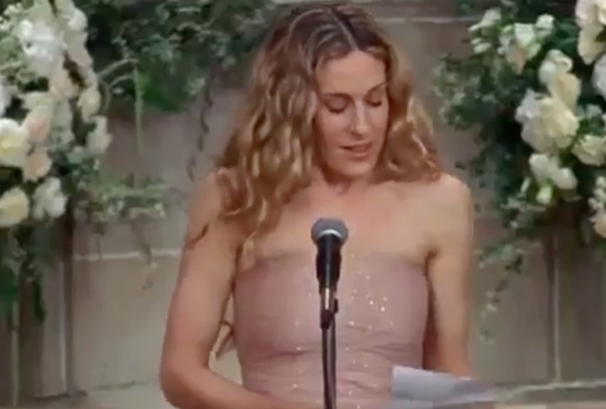 Carrie wears a sparkly dress and reads from a sheet of paper in front of a microphone