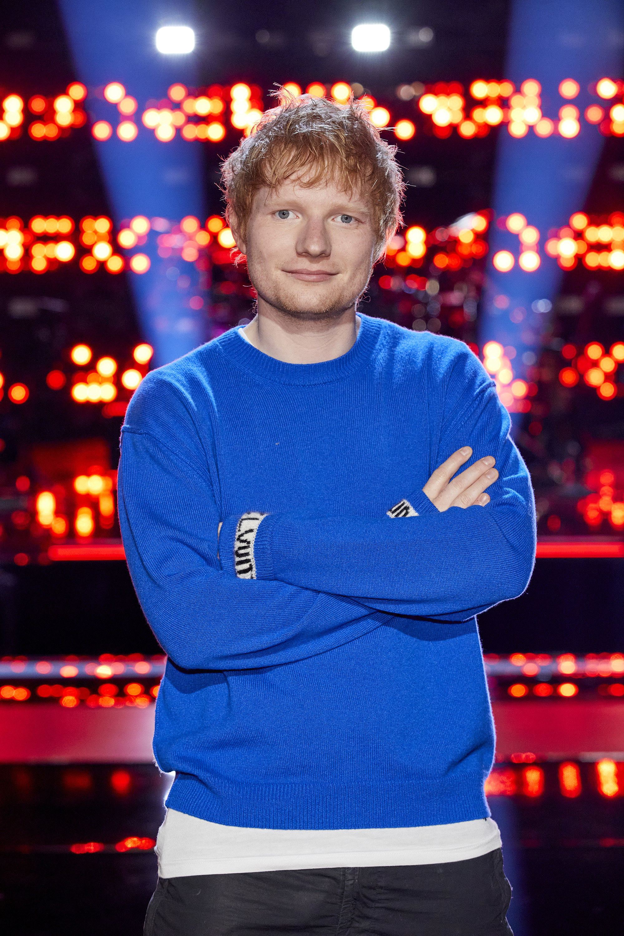 Sheeran stands while facing a camera with his arms crossed