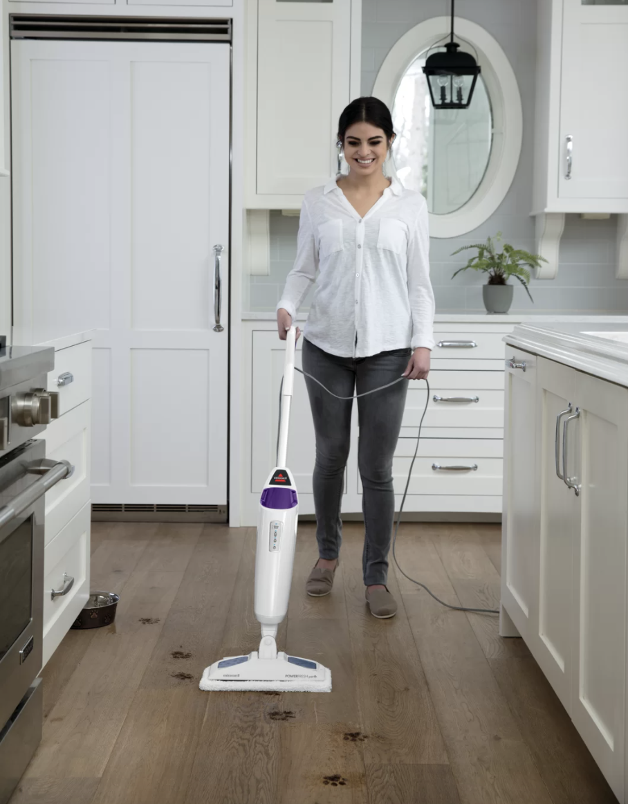 A person uses the steam cleaner in the kitchen to remove dirty paw prints from the floor