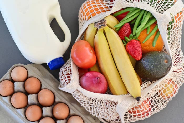 A half gallon of milk, a carton of eggs, and a shopping bag of fresh fruits and vegetables