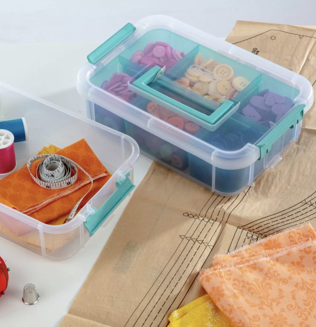 They clear and teal stacked organizational boxes are holding buttons and other sewing supplies