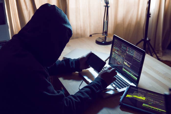 Hacker in a hoodie using a smartphone and laptop